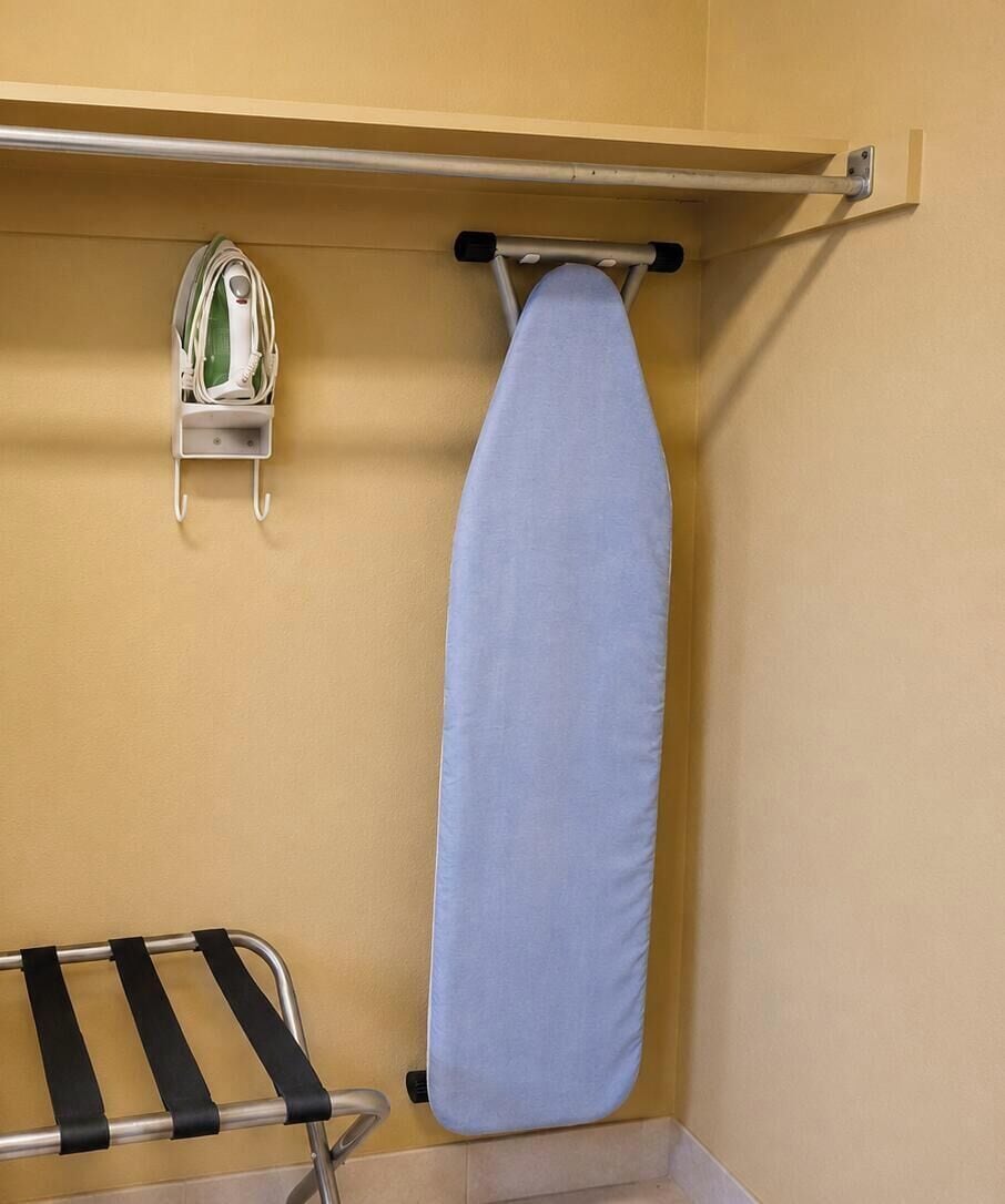 A corner of a room with a hanging ironing board and an iron on the wall.