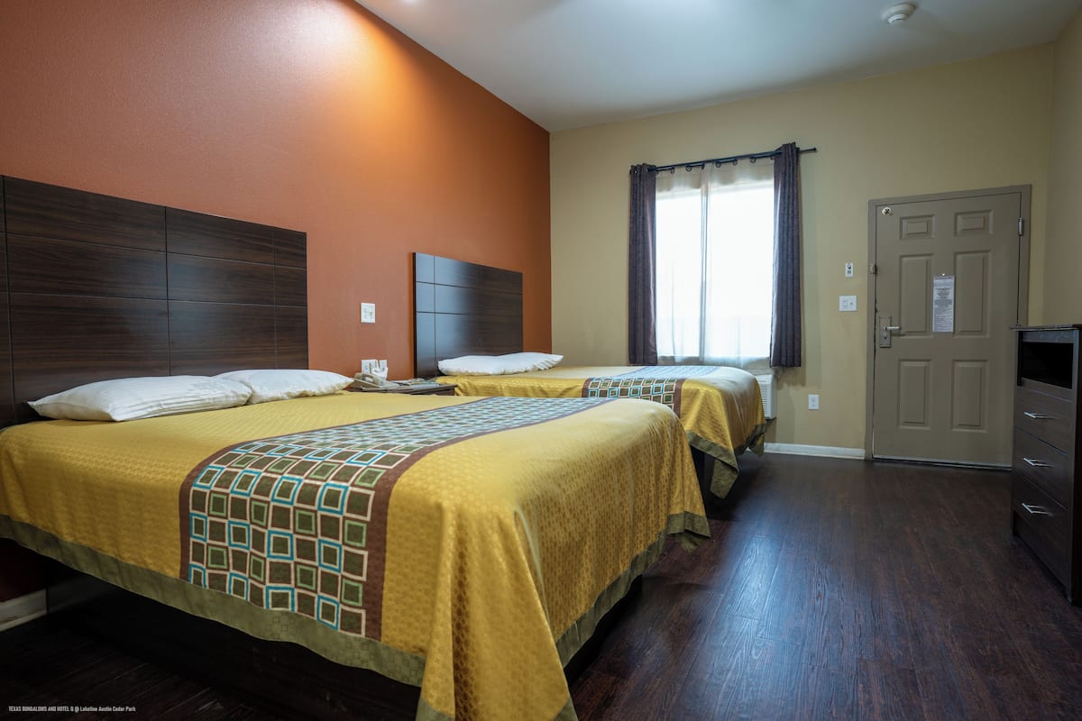 Habitación de hotel con dos camas, cabecero de madera, ventana con cortinas, una puerta y un televisor de pantalla plana.