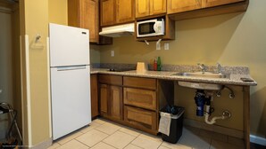 A kitchen with wooden cabinets, a white refrigerator, a built-in microwave, a sink, and a trash can. - Texas Bungalows Hotel & Hotel Que at Lakeline Austin Cedar Park (Cedar Park)