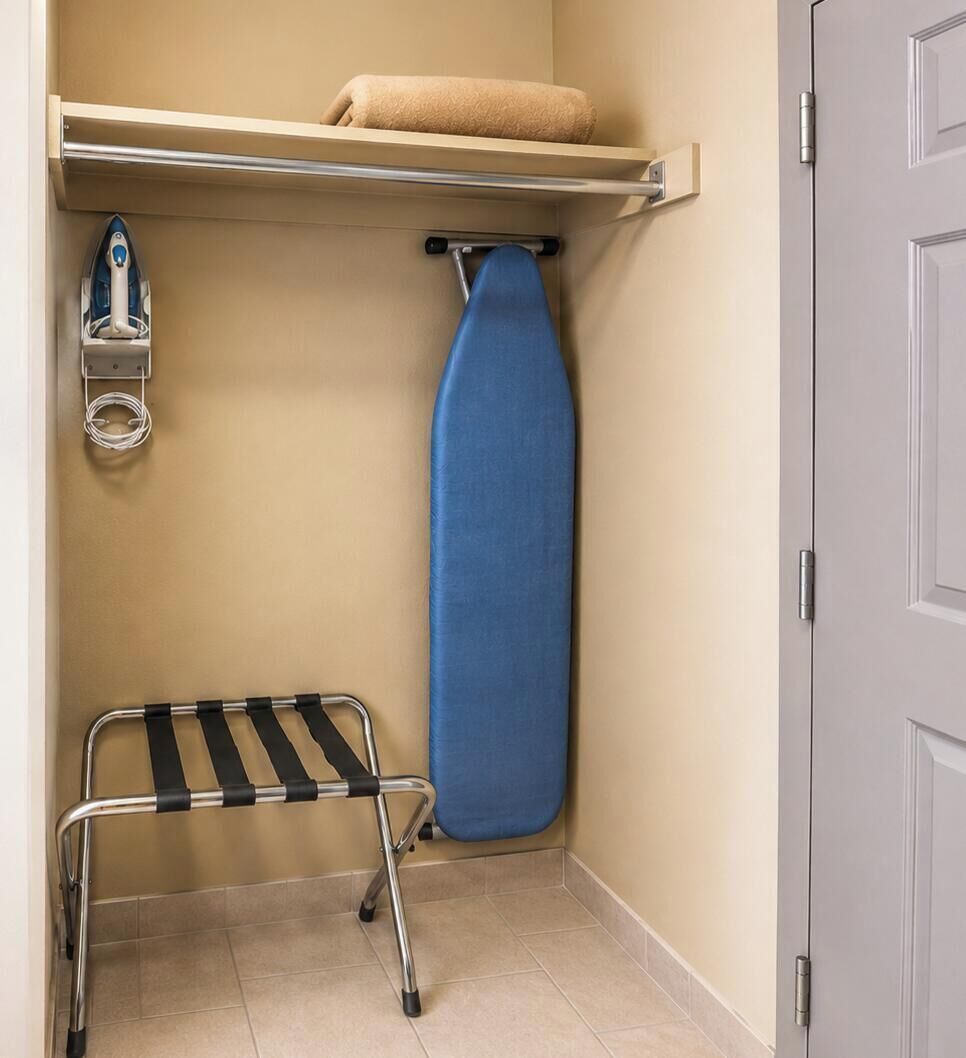 Une petite pièce utilitaire comprenant un fer à repasser suspendu, une planche à repasser bleue et une étagère sur laquelle est posée une serviette enroulée.