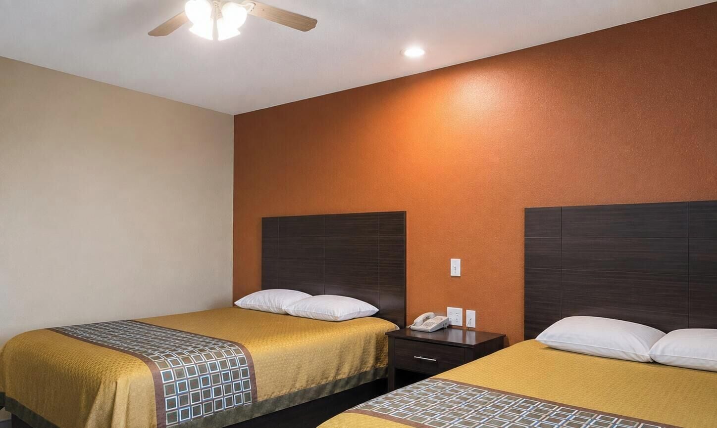 A hotel room with two beds, a nightstand, and a ceiling fan.