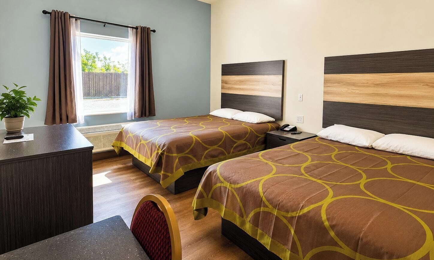 A hotel room with two beds, a desk, and a window with curtains.