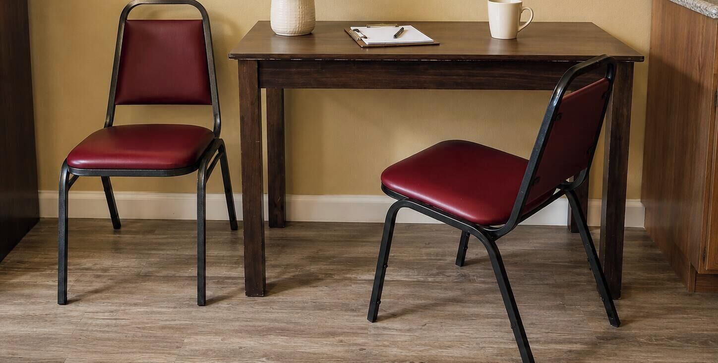 Dos sillas rojas con estructura metálica y una mesa de madera con una taza blanca y un cuaderno.