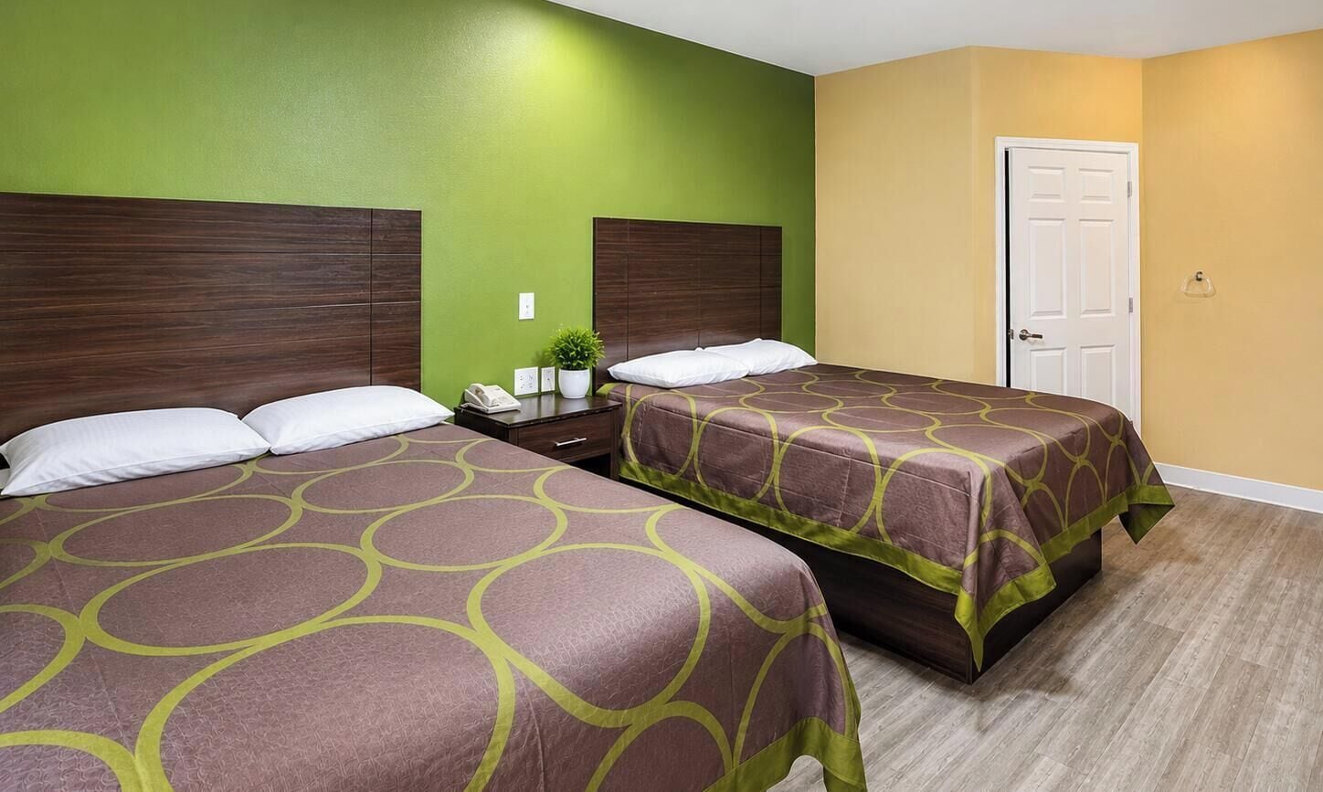 A hotel room with two beds, a wooden headboard, a green wall, a yellow wall, and a wooden floor.