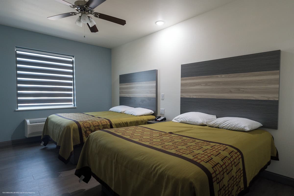 Habitación de hotel con dos camas, ventilador de techo, ventana con persianas y teléfono montado en la pared.