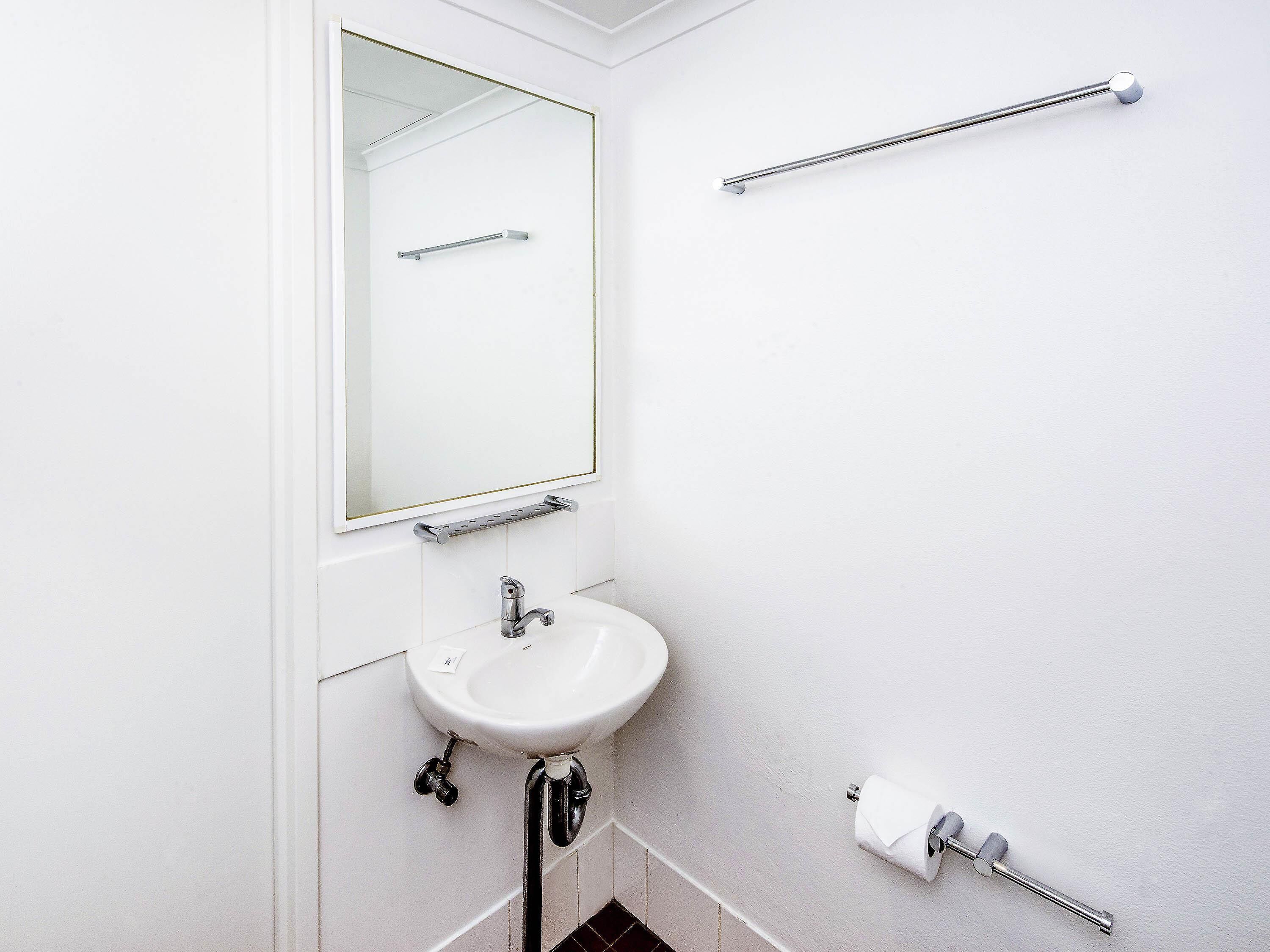 A bathroom with a sink, mirror, towel rack, and toilet paper holder.
