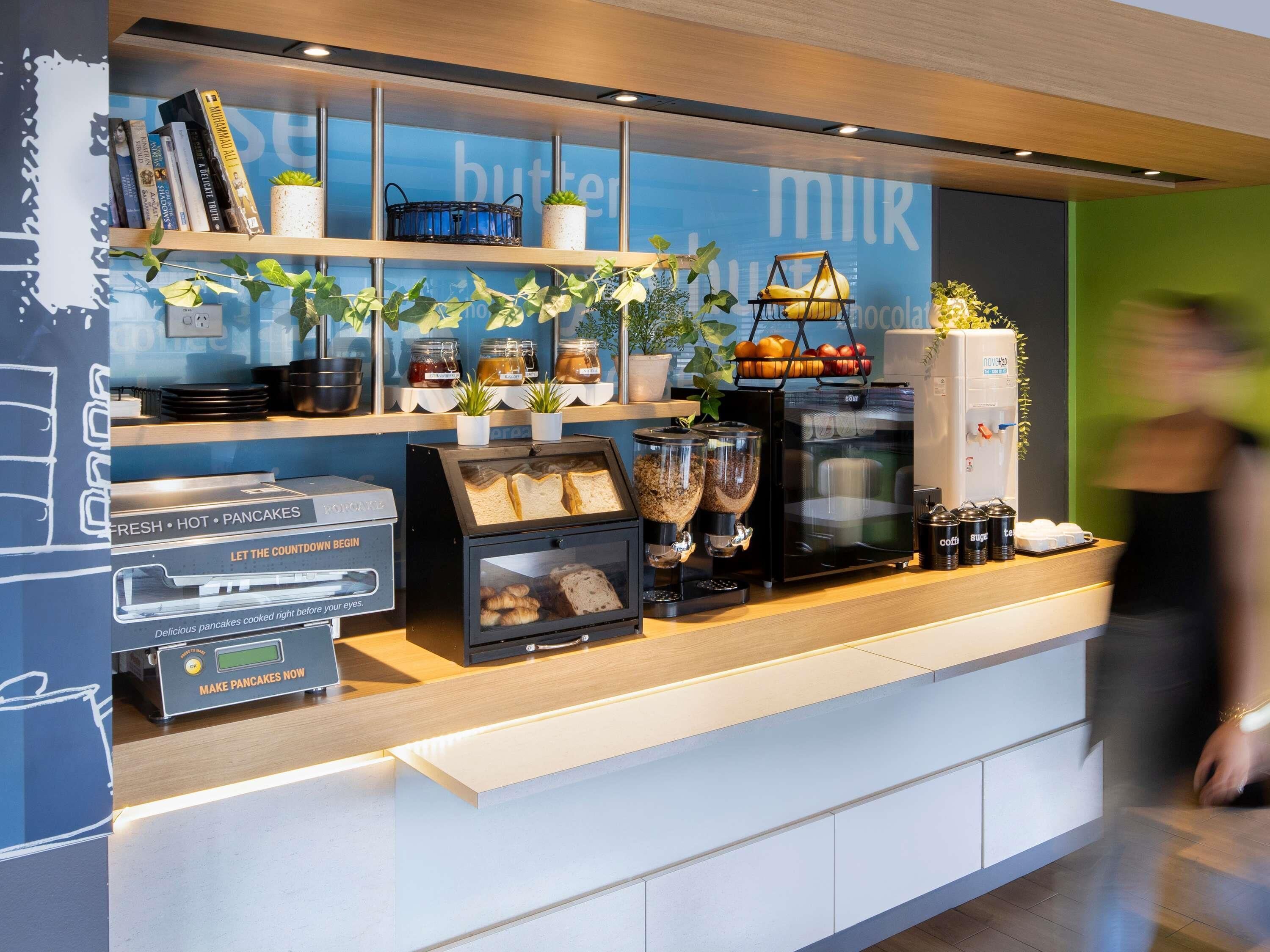 A breakfast counter with a coffee machine, bread, pastries, and a sign that says 'fresh hot pancakes.'