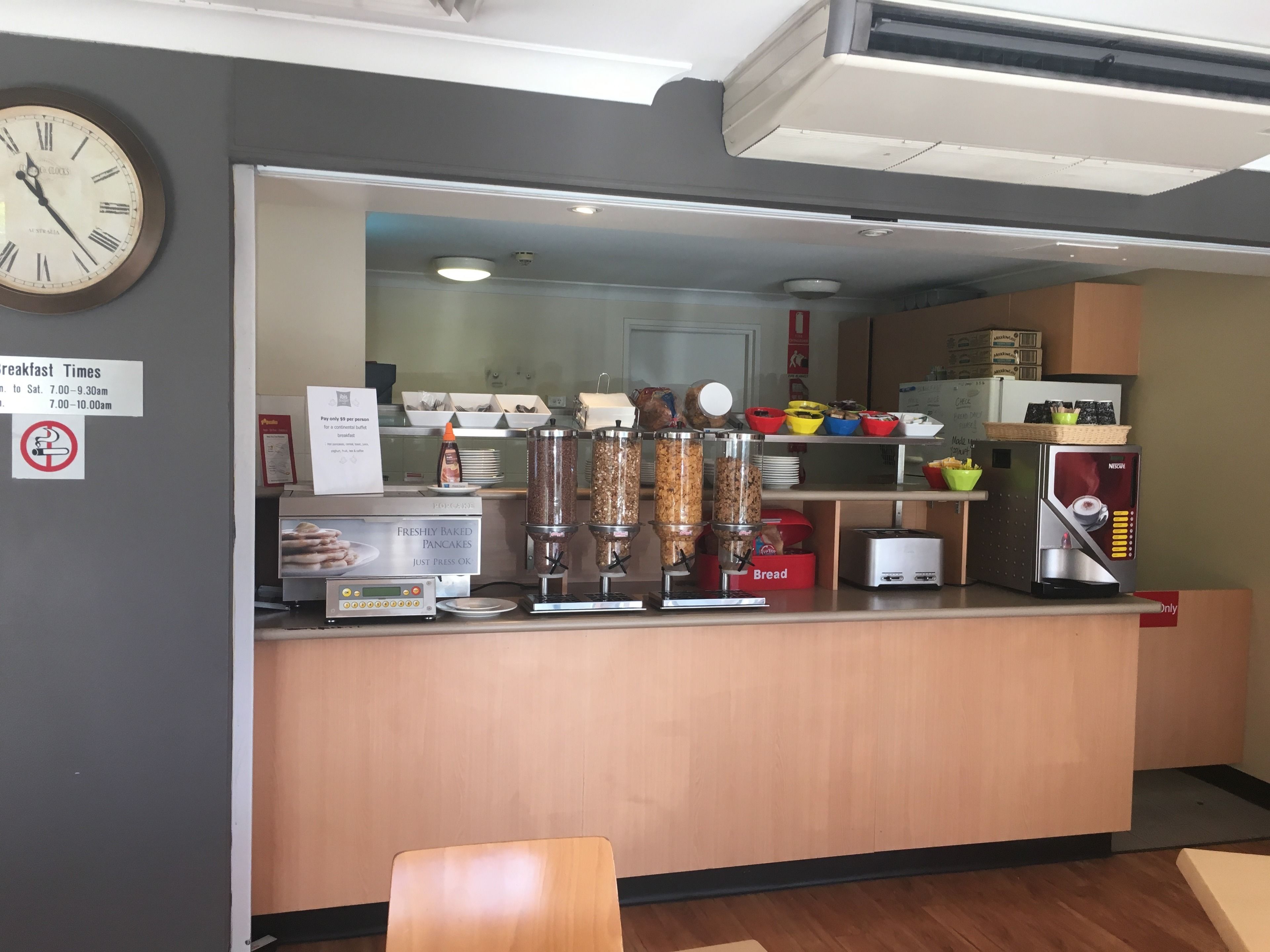 A breakfast counter with a clock, a sign indicating breakfast times, and various food dispensers.