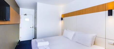 Una habitación de hotel moderna con una cama grande, un televisor de pantalla plana montado en la pared y un cabecero de madera.