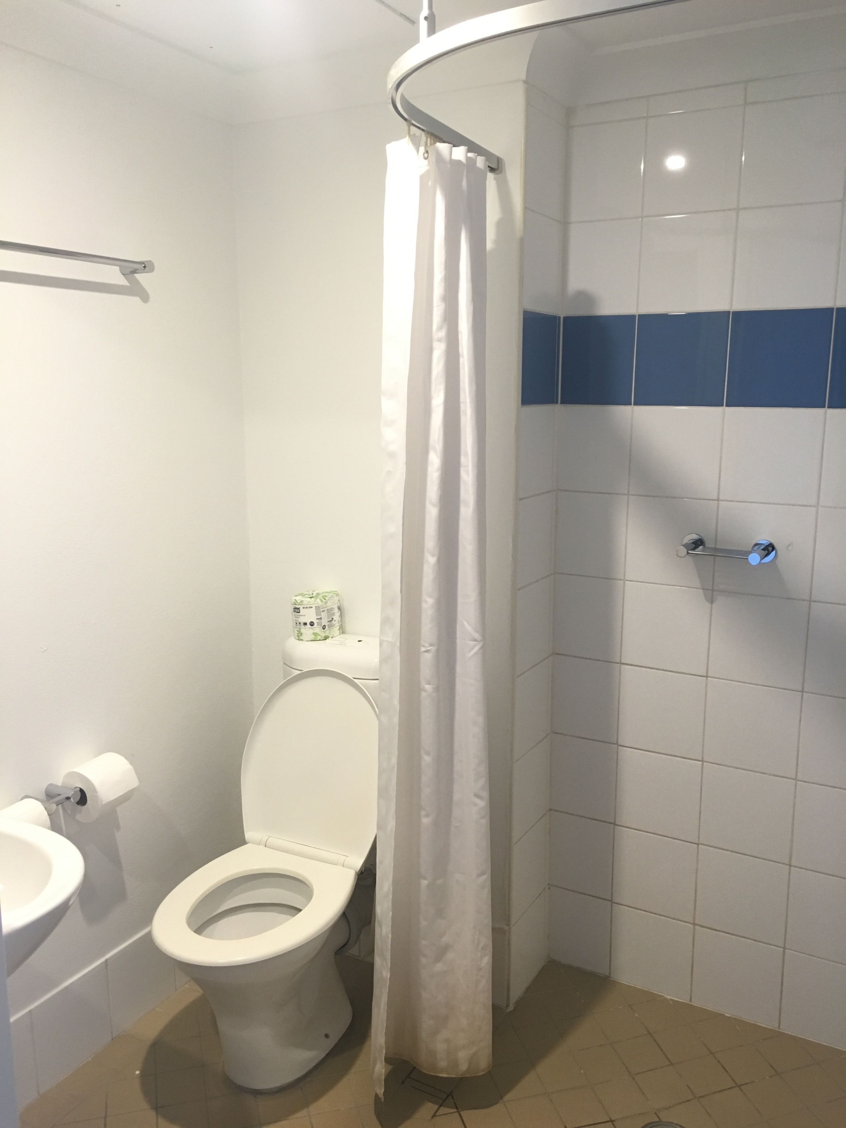 A bathroom with a toilet, a shower curtain, and a towel rack.