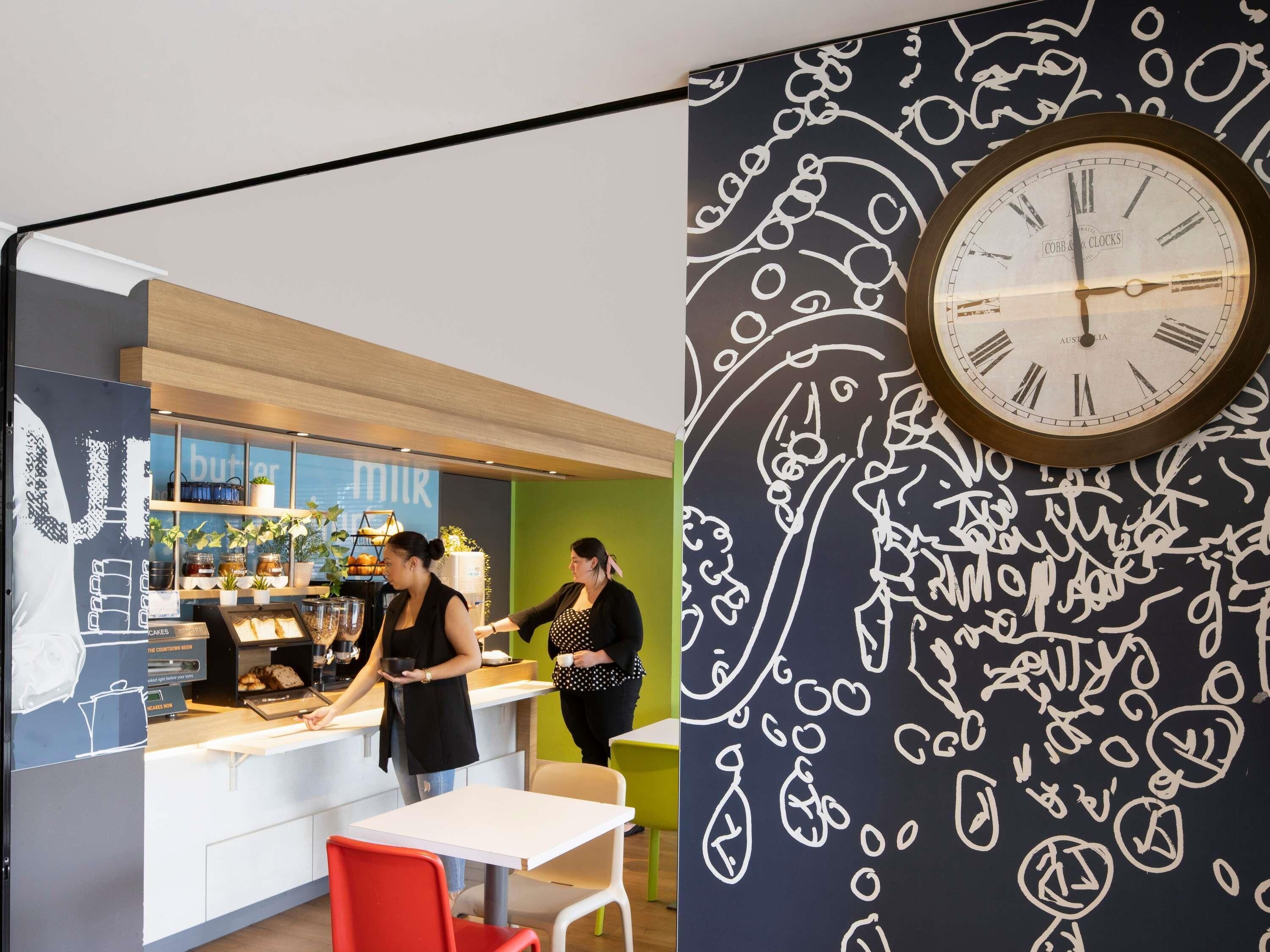 L’intérieur d’un café, avec un comptoir, un espace salon et une horloge murale.