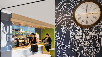 L’intérieur d’un café, avec un comptoir, un espace salon et une horloge murale.