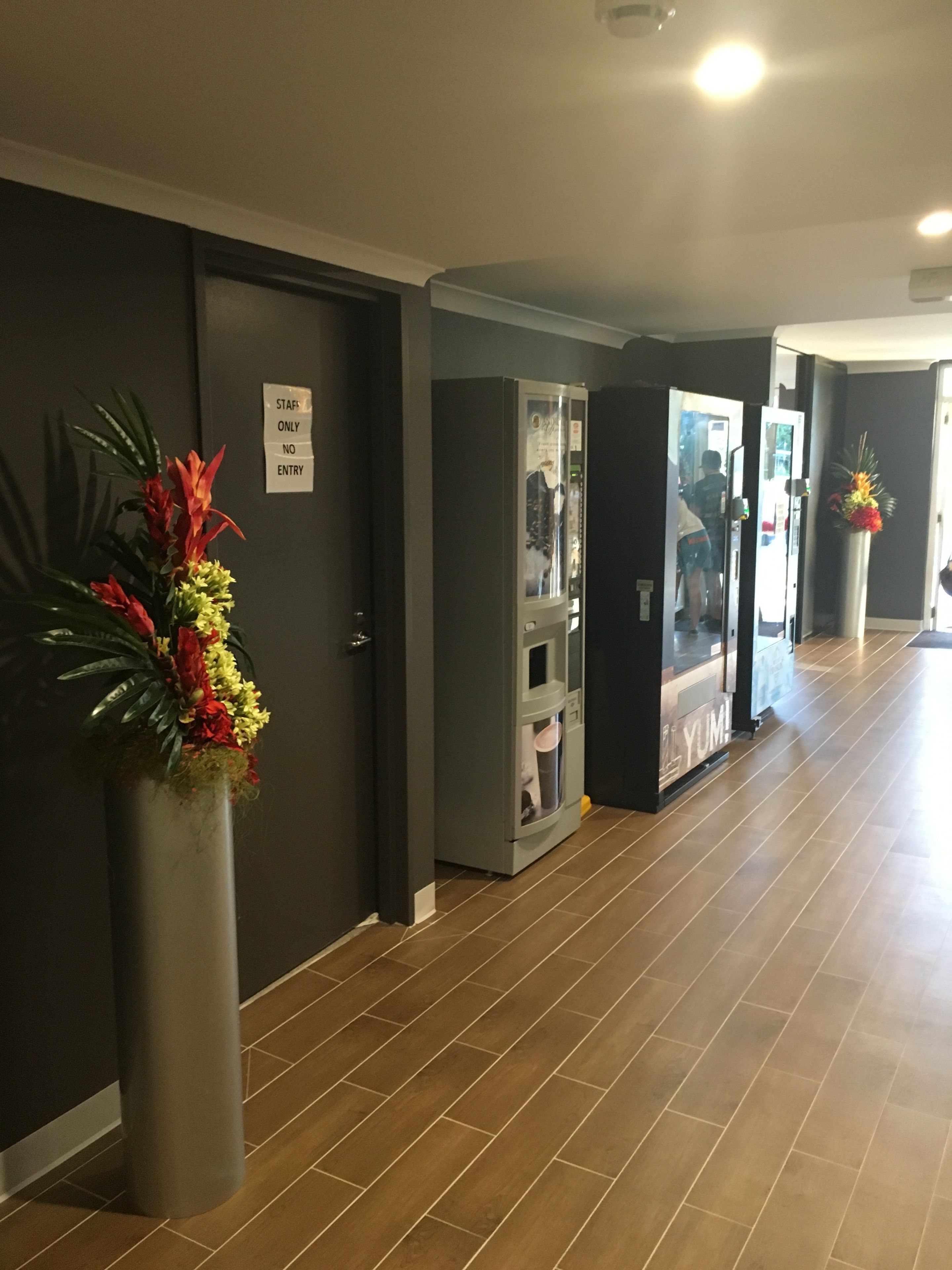 Ein Hotelkorridor mit einem Getränkeautomaten, einer Tür für Mitarbeiter und einer Blumenvase.