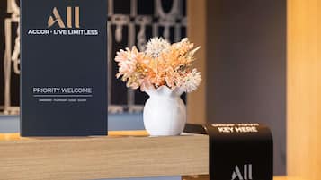Un mostrador de recepción con un cartel que dice 'Priority Welcome', un jarrón blanco con flores y un cartel que indica 'Key Here'.