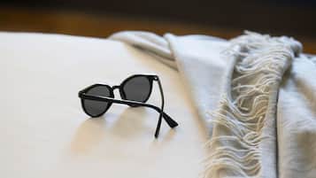 Un par de gafas de montura negra sobre una superficie blanca, con una manta gris texturizada a su lado.