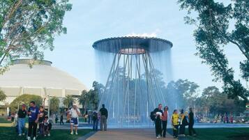 A public park with a large fountain in the center, surrounded by trees and a crowd of people.