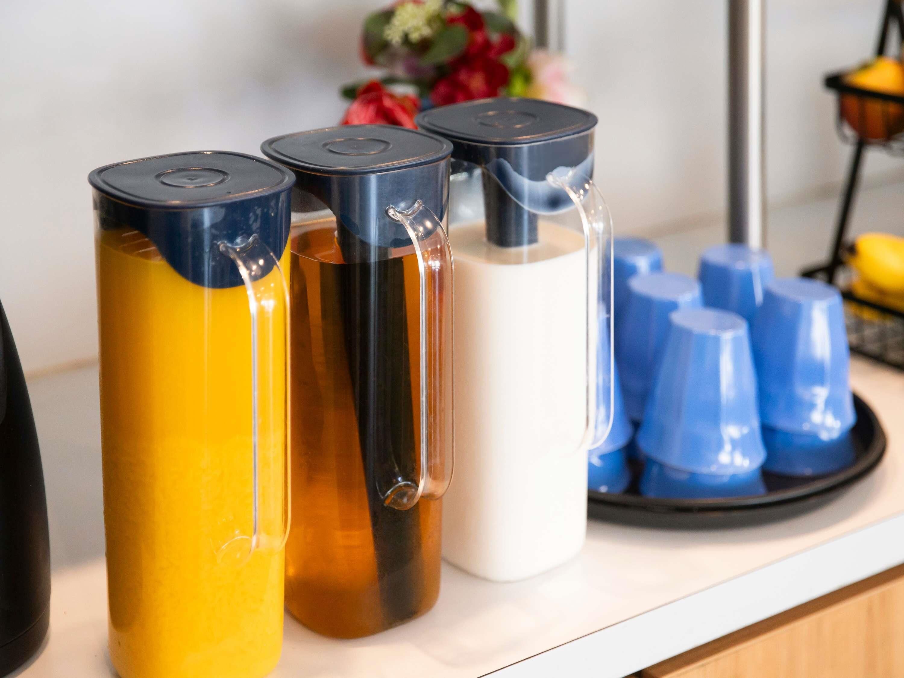 A counter with three beverage dispensers in different colors and a tray with blue cups.