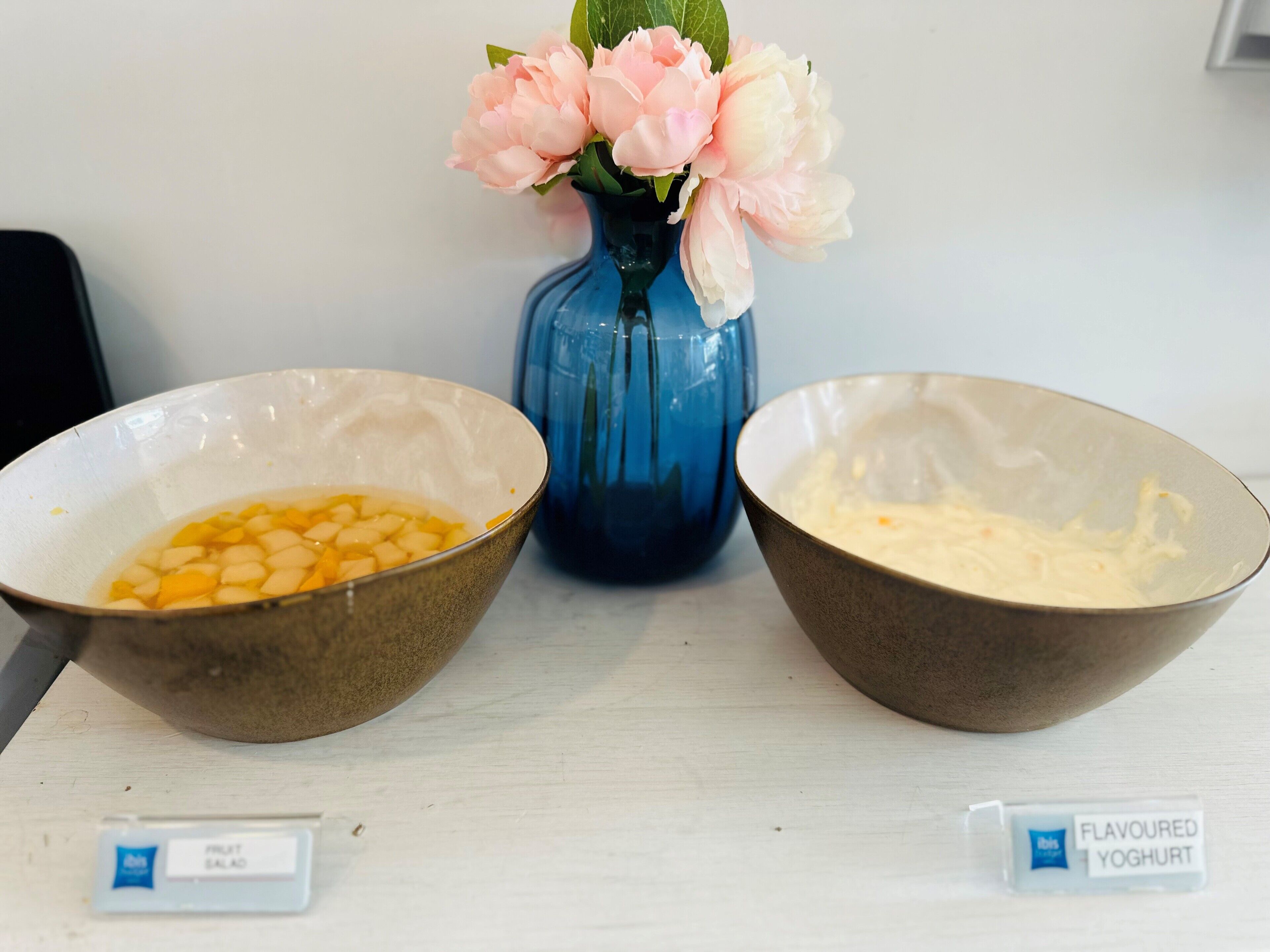 Two bowls of food on a table with a blue vase of flowers in the background.