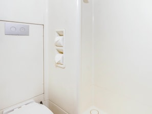 A bathroom with a toilet, a wall-mounted light switch, and a towel rack.