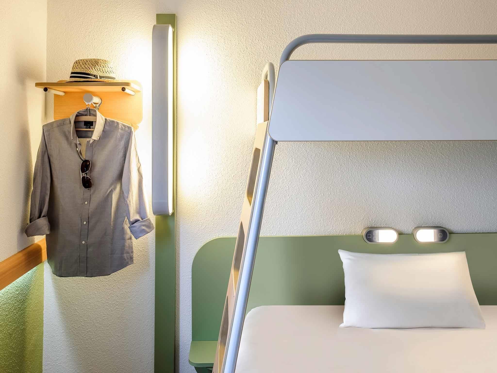 A bunk bed with a pillow and a hanging garment rack with a hat and a shirt.