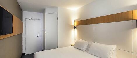 A hotel room with a bed, a television mounted on the wall, and a door leading to a bathroom.