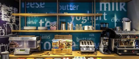 A café counter with a coffee machine, a display of freshly baked pancakes, and various food items.