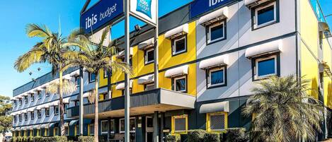 A modern hotel building with multiple balconies and a prominent 'ibis budget' sign.
