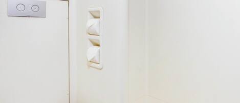 A bathroom with a toilet, a wall-mounted light switch, and a towel rack.