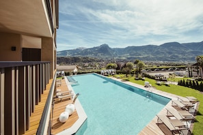 A pool with wooden deck and lounge chairs, surrounded by mountains and a view of a town. - La Maiena Meran Resort (Marlengo)