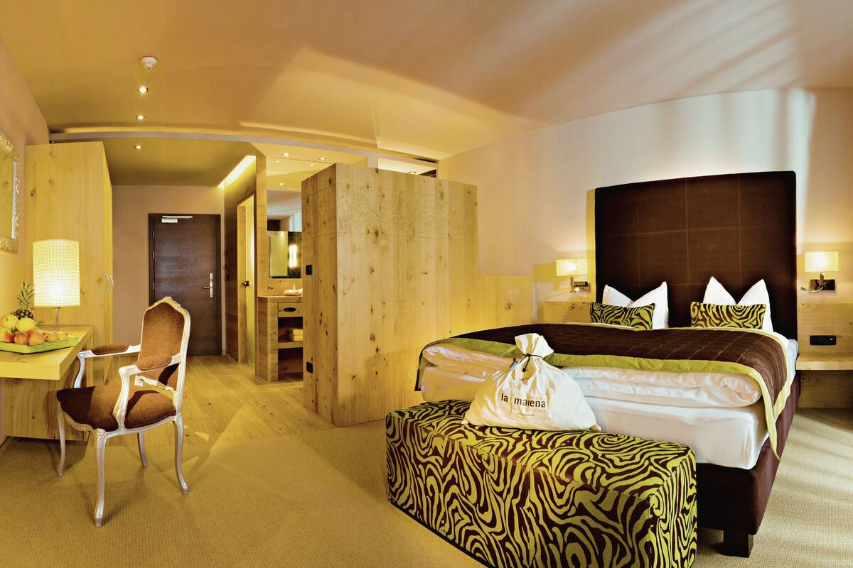Ein Hotelzimmer mit Bett, Schreibtisch, Stuhl, einem kleinen Tisch mit Obst und einem durchgegangene Tür erkennbaren Badezimmer.