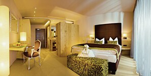 A hotel room with a bed, a desk, a chair, a small table with fruit, and a bathroom visible through an open door. - La Maiena Meran Resort (Marlengo)