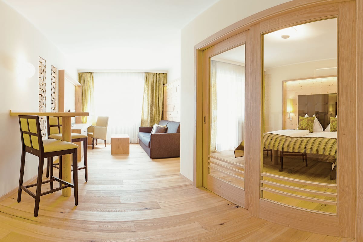 Ein modernes Hotelzimmer mit Holzboden, einer Couch, einem Essbereich mit Stühlen und einem großen Spiegel.