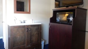 A bathroom with a wooden vanity, a mirror, a sink, a microwave, and a television. - Citilodge Suites (Missoula)