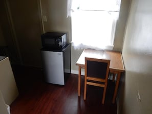 Une cuisine compacte équipée d’un réfrigérateur, d’un four à micro-ondes et d’une petite table en bois avec une chaise.