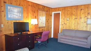 A room with wooden paneling, a television on a wooden desk, a chair, a sofa, and a door. - Citilodge Suites (Missoula)