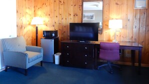 A room with wooden panel walls, a television on a black stand, a microwave, a small refrigerator, a striped armchair, a purple office chair, and a desk with a lamp. - Citilodge Suites (Missoula)