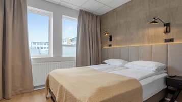 A modern hotel room with a large bed, a nightstand, a wall-mounted lamp, and a window with curtains.