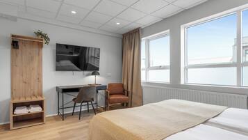 Una habitación de hotel moderna con cama, escritorio, silla, armario y una ventana grande.