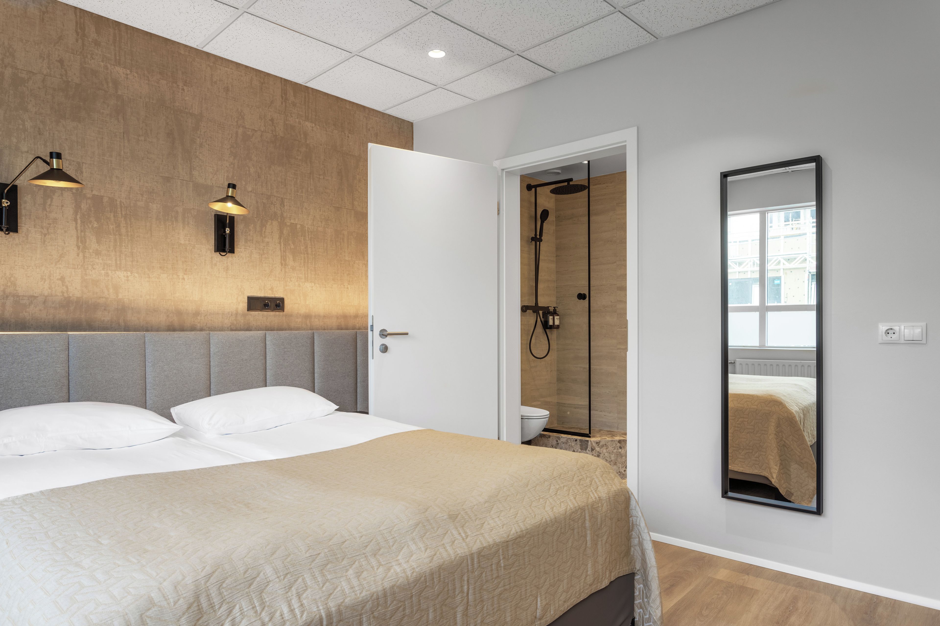 A modern hotel room with a large bed, a shower area, and a mirror reflecting the bed.