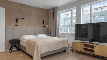 Habitación de hotel moderna con una cama grande, un televisor sobre una consola de madera y una ventana con vista a la ciudad.