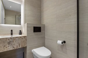 Un baño moderno con lavabo de mármol, inodoro y cabina de ducha con mampara de vidrio.