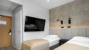 Habitación de hotel con dos camas individuales, un televisor montado en la pared y dos lámparas de pared.