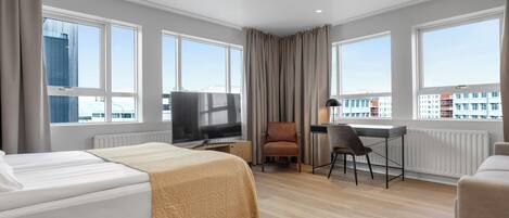 A hotel room with a bed, a desk, a chair, a television, and large windows with a city view.