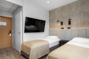 Habitación de hotel con dos camas, un televisor montado y dos lámparas fijadas a la pared.