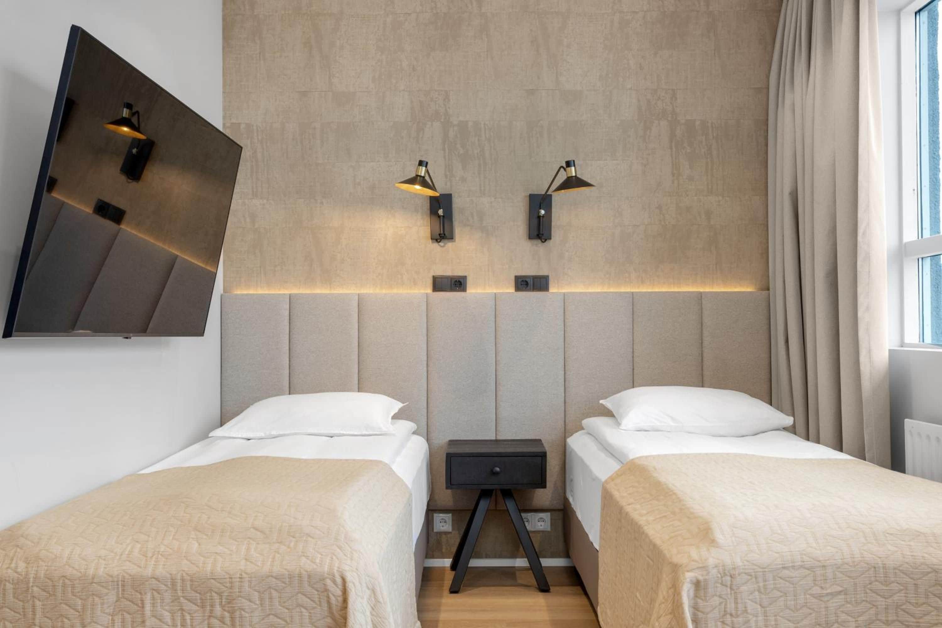 Ein Hotelzimmer mit zwei Betten, einem wandmontierten Fernseher und zwei Wandlampen.