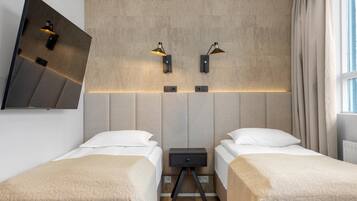 A hotel room with two beds, a wall-mounted TV, and two wall-mounted lamps.