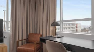 Una habitación de hotel moderna con un ventanal grande, un escritorio, una silla y un televisor.
