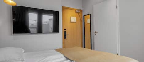 A hotel room with a bed, a window, a door, and a wall-mounted mirror.