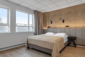 A modern hotel room with a large bed, a nightstand, and a view of the city through the window. - Alva Hotel Brautarholt (Reykjavik)