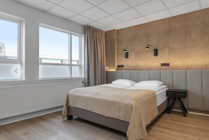 Una camera d'albergo moderna con un letto grande, un comodino e vista sulla città dalla finestra.